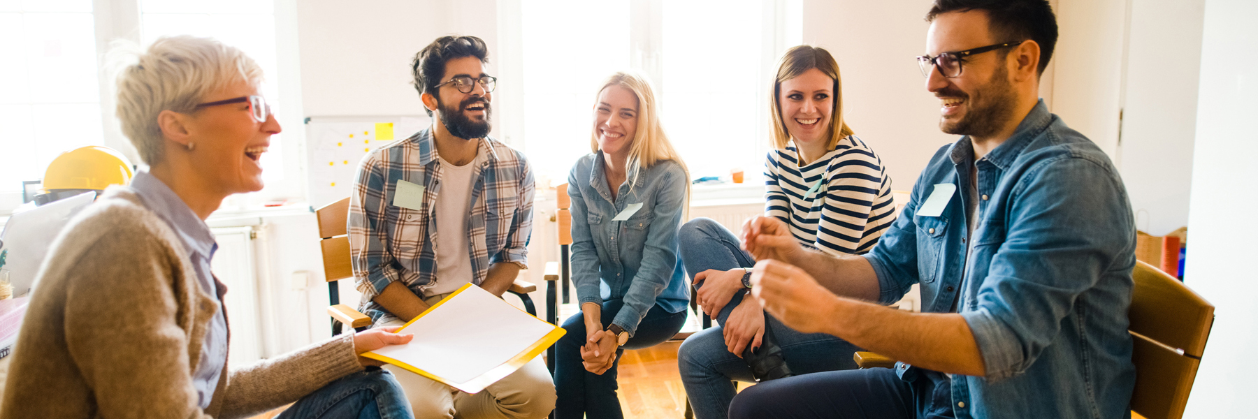 Dozent_Dozentin Das Bild zeigt fünf Menschen in Workshop-Atmosphäre. Sie sitzen lachend im Kreis.